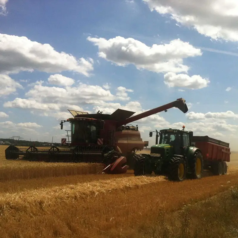 Photo d'un champ travaillé par un tracteur et suivi d'un silo sur un camion